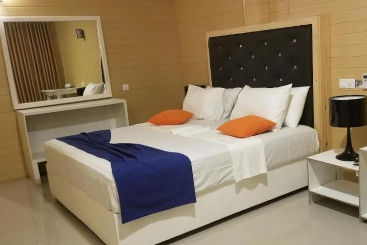 Una habitación de hotel con una cama, mesitas de noche, una lámpara y un espejo.