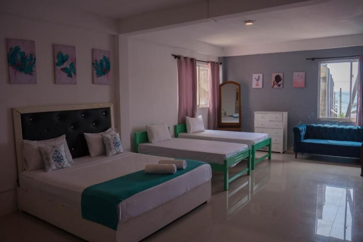 Habitación de hotel con dos camas, un aparador, un espejo y un sofá azul.