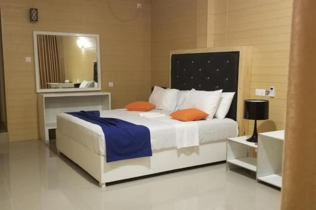Una habitación de hotel con cama, mesita de noche, lámpara y espejo.