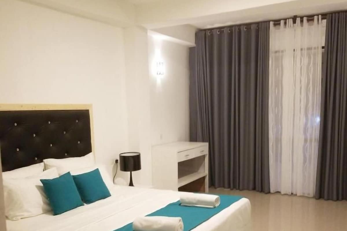 Habitación de hotel con cama, mesita de noche, escritorio y ventana con cortinas.