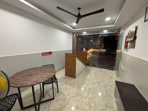 Un vestíbulo de hotel con una recepción, una mesa redonda con sillas, un ventilador de techo y un piso de mármol.