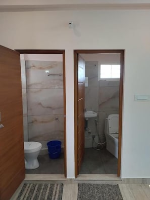 Un baño con inodoro, un cubo azul y una zona de ducha.