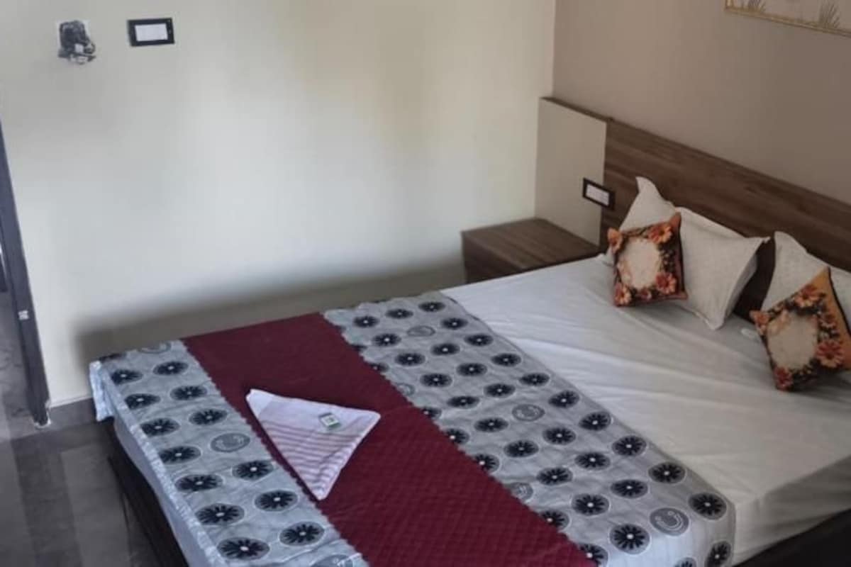 Una cama con colcha estampada, almohadas y una mesita de noche con lámpara.
