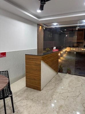 Un área de recepción con un mostrador de madera, un separador de vidrio y un piso de mármol.