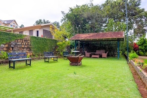 A well-maintained garden with a stone wall, a covered seating area, and outdoor furniture. - 42 Green Pastures Tea Estate Experience (Araihatty)