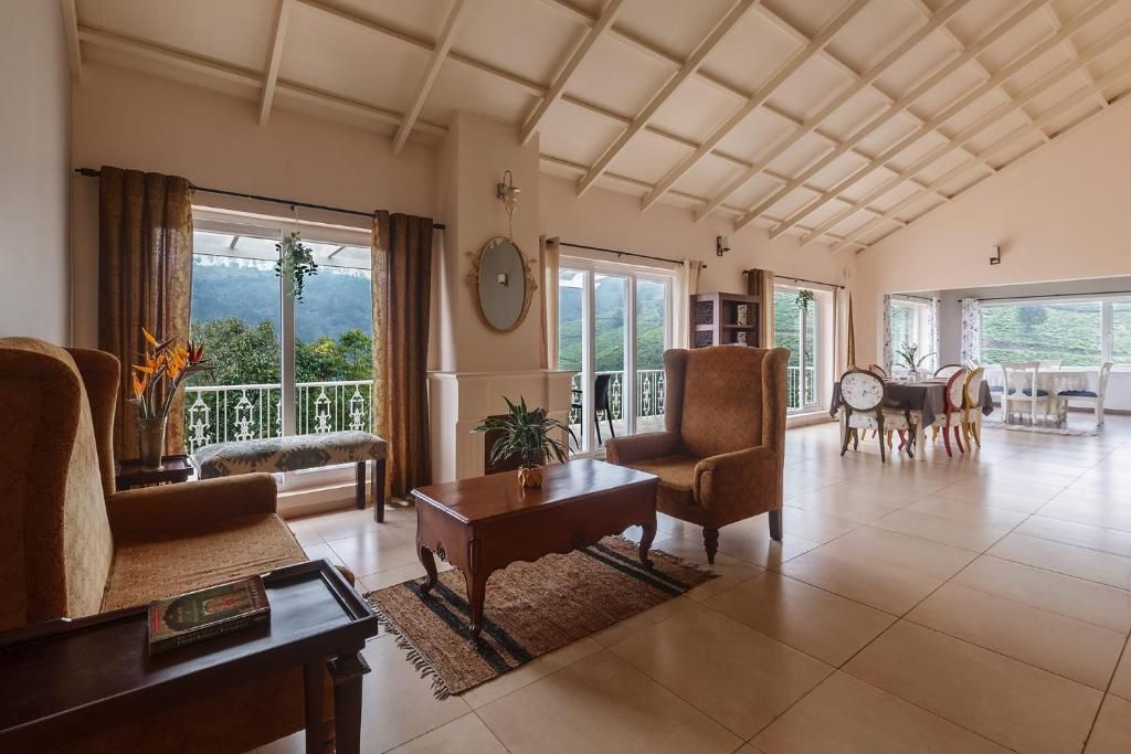 A spacious living room with a high ceiling, large windows, a dining area, and a view of greenery.