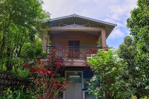 A two-story building with a balcony, surrounded by lush greenery and a clear sky. - 42 Green Pastures Tea Estate Experience (Araihatty)