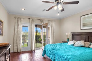 Un dormitorio con una cama, ventilador de techo, ventana con cortinas y vistas al exterior.