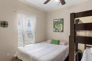 Un dormitorio con una cama, un ventanal con persianas, un ventilador de techo y una obra de arte colgada en la pared.