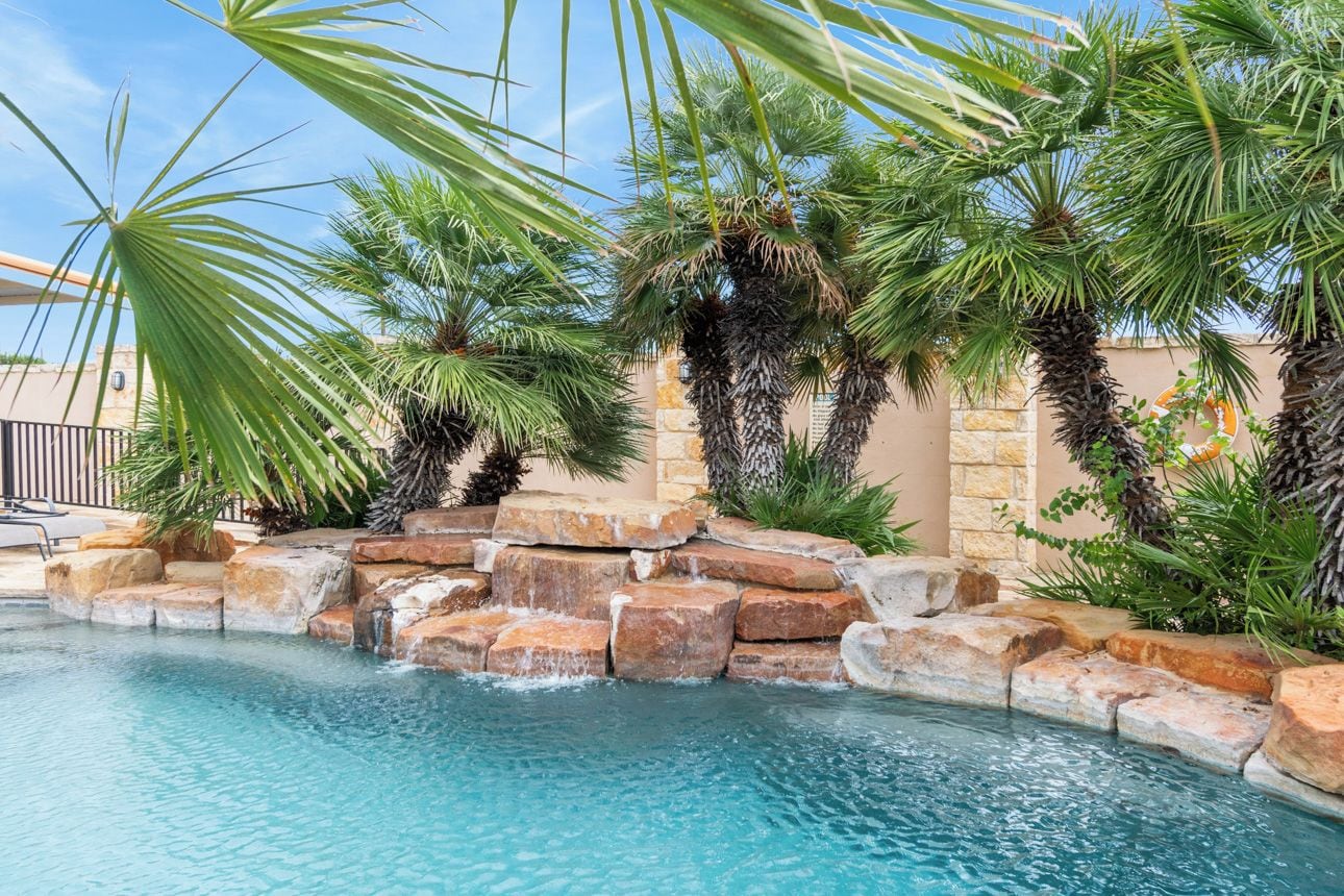 Una piscina con palmeras y un muro de piedra.