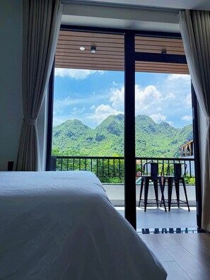Una habitació d'hotel amb un llit gran, un balcó amb vistes a muntanyes verdes i una cadira.