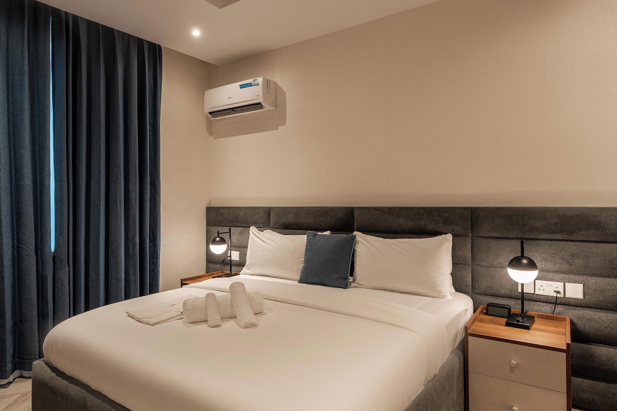 Quarto de hotel moderno com uma cama grande, mesas de cabeceira, ar condicionado e uma janela com cortinas.