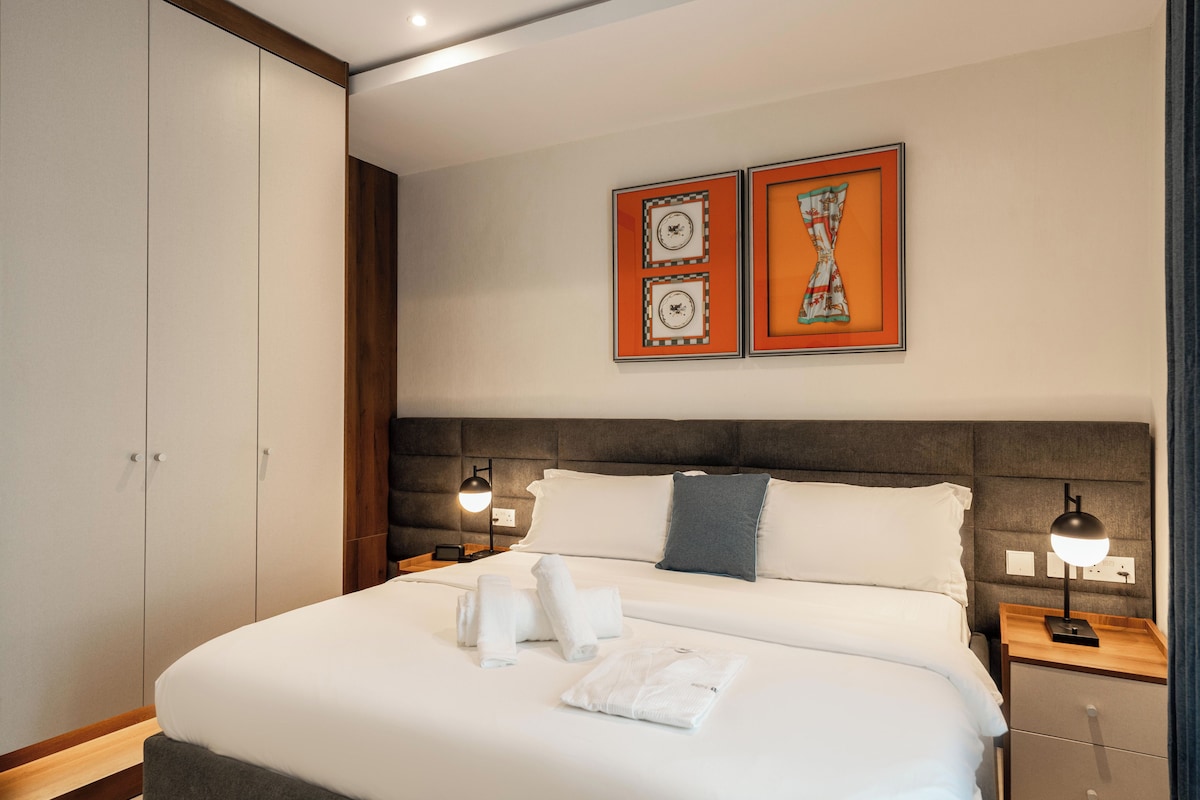 Quarto de hotel com uma cama grande, duas mesas de cabeceira, uma cabeceira e duas pinturas penduradas na parede.