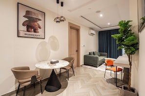 Uma sala de estar moderna com sofá, mesa de jantar com cadeiras, planta em vaso e um cartaz na parede.