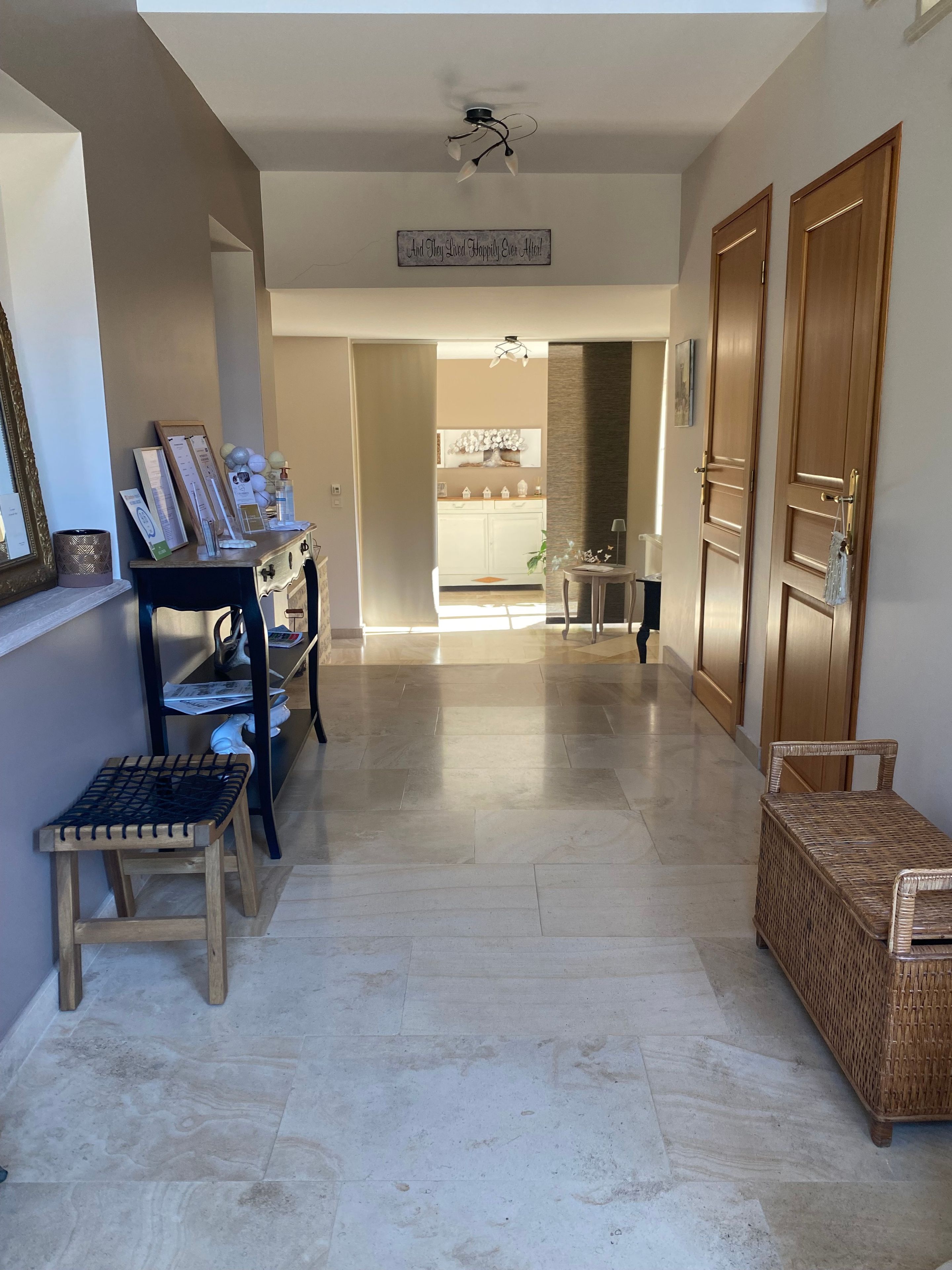 Un couloir avec un ventilateur de plafond, un panneau indicateur, un bureau avec des papiers, un banc et une chaise en osier.