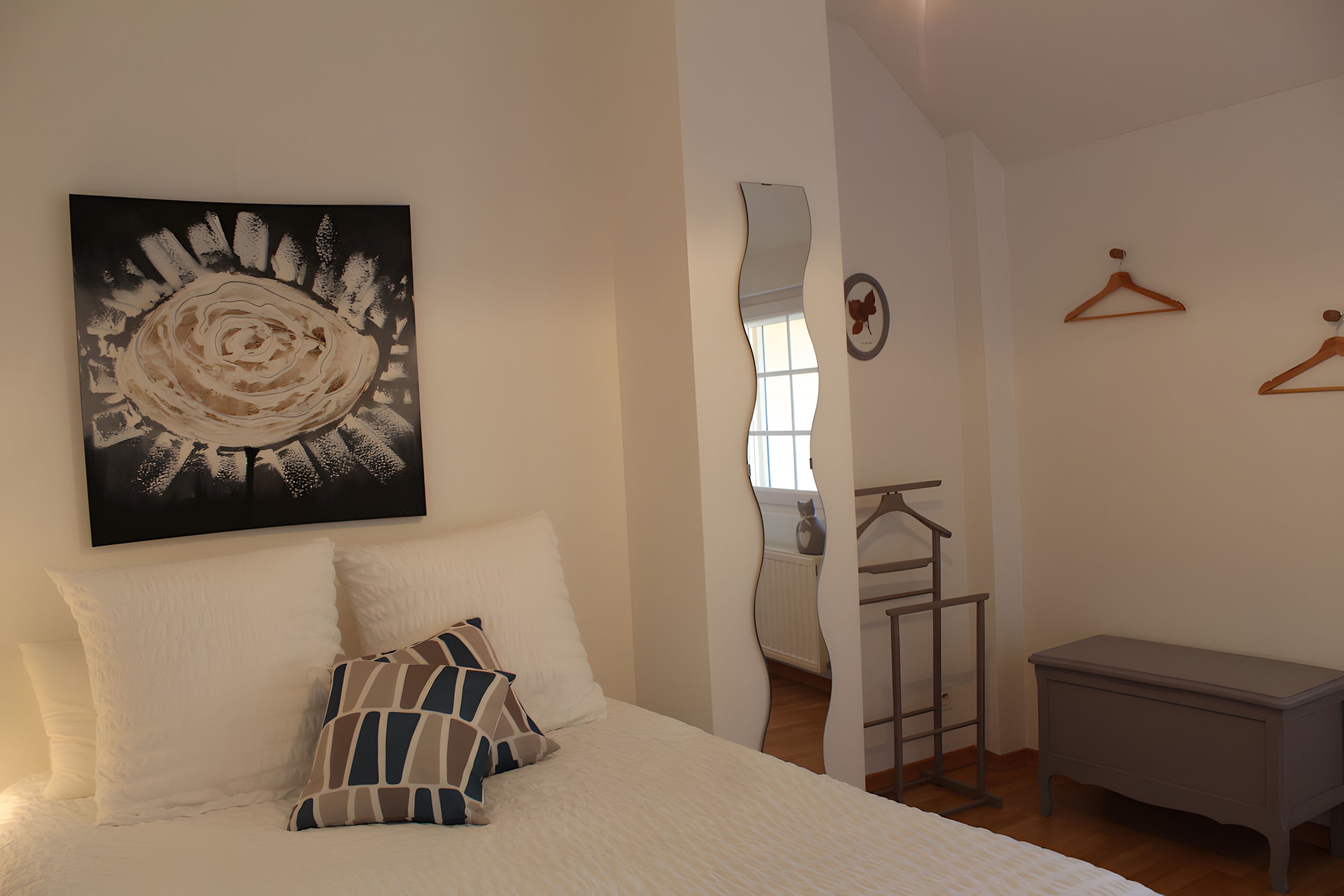 Une chambre à coucher comprenant un lit, des oreillers, une commode, un miroir et une œuvre d’art accrochée au mur.
