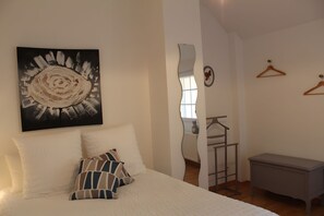 Une chambre à coucher comprenant un lit, des oreillers, une commode, un miroir et une œuvre d’art accrochée au mur.