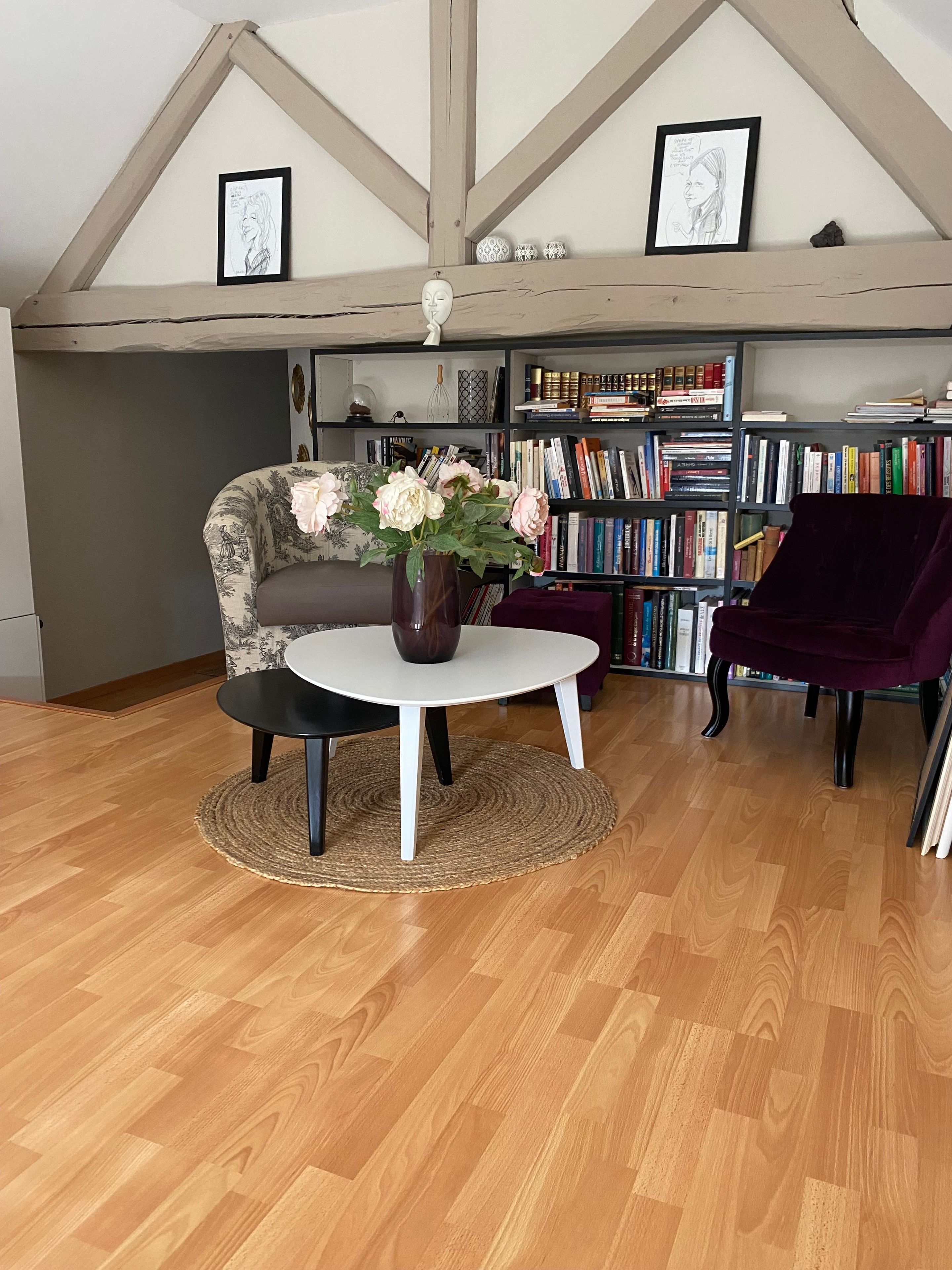 Une pièce chaleureuse avec un plancher en bois, une table ronde ornée d’un vase de fleurs, un canapé et une bibliothèque remplie de livres.