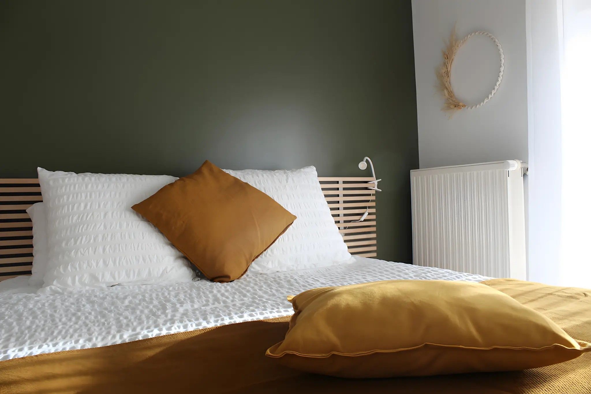Un lit avec une literie blanche et marron, une tête de lit en bois et un radiateur blanc.