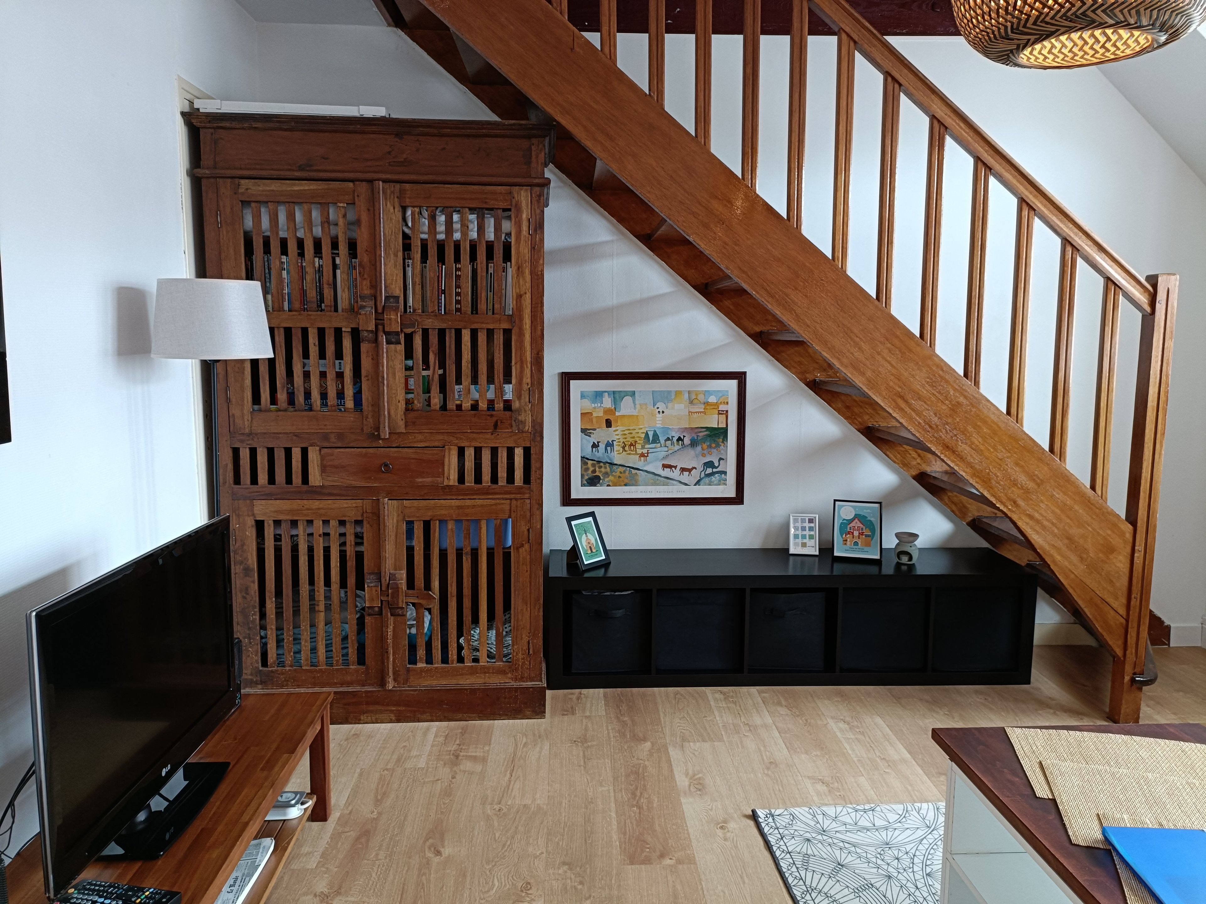 Una escalera con barandillas de madera, un televisor de pantalla plana, un mueble de madera con libros y un cuadro en la pared.