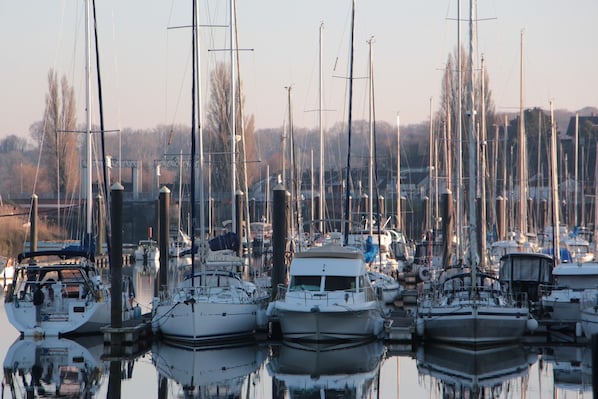 En lysthavn med flere både i havnen, stille vand og en bro i baggrunden.