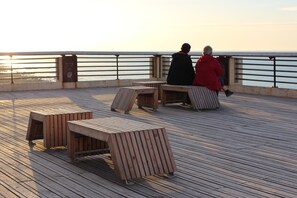En træterrasse med bænke og borde, med udsigt over vandet.