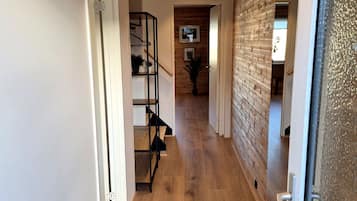 Un couloir doté d’un plancher en bois, d’un escalier avec des rampes en métal et d’une porte ornée d’un panneau de verre texturé.