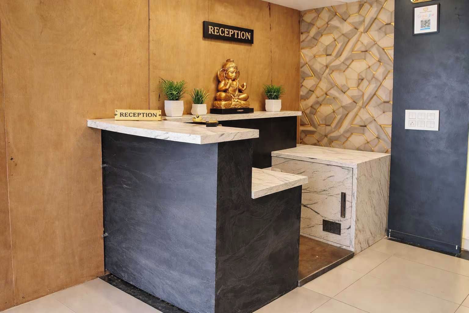 A reception desk with a sign, a Buddha statue, and two potted plants.
