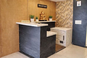 A reception desk with a sign, a Buddha statue, and two potted plants. - Hotel O Bada Ganpati Indore Airport (Indore)