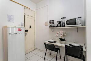 Een kleine kitchenette met een koelkast, magnetron, koffiezetapparaat en een losse stoel.