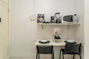 Een kleine kitchenette met een magnetron, koffiezetapparaat en een bordje met de tekst 'Cantinho do'. Op het aanrecht staan twee stoelen en een potplant.