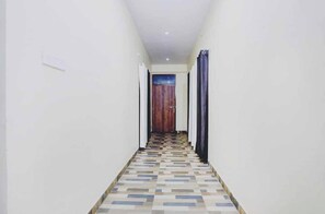 A narrow hallway with a patterned floor, white walls, and a wooden door at the end. - Hotel O IIT Banaras Road (Varanasi)