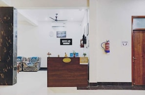A hotel reception area with a wooden reception desk, a ceiling fan, a fire extinguisher, and a sign indicating the entrance. - Hotel O IIT Banaras Road (Varanasi)