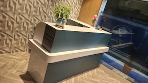 A reception desk with a modern design, a potted plant, and a poster advertising a hotel. - Collection O Bandra Terminus (Mumbai)