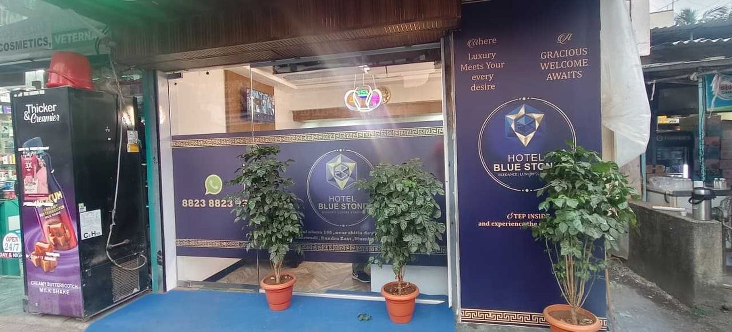A hotel entrance with a blue sign, potted plants, and a creamery advertisement.