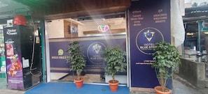 Entrada de hotel con un letrero azul, plantas en macetas y un anuncio de heladería.