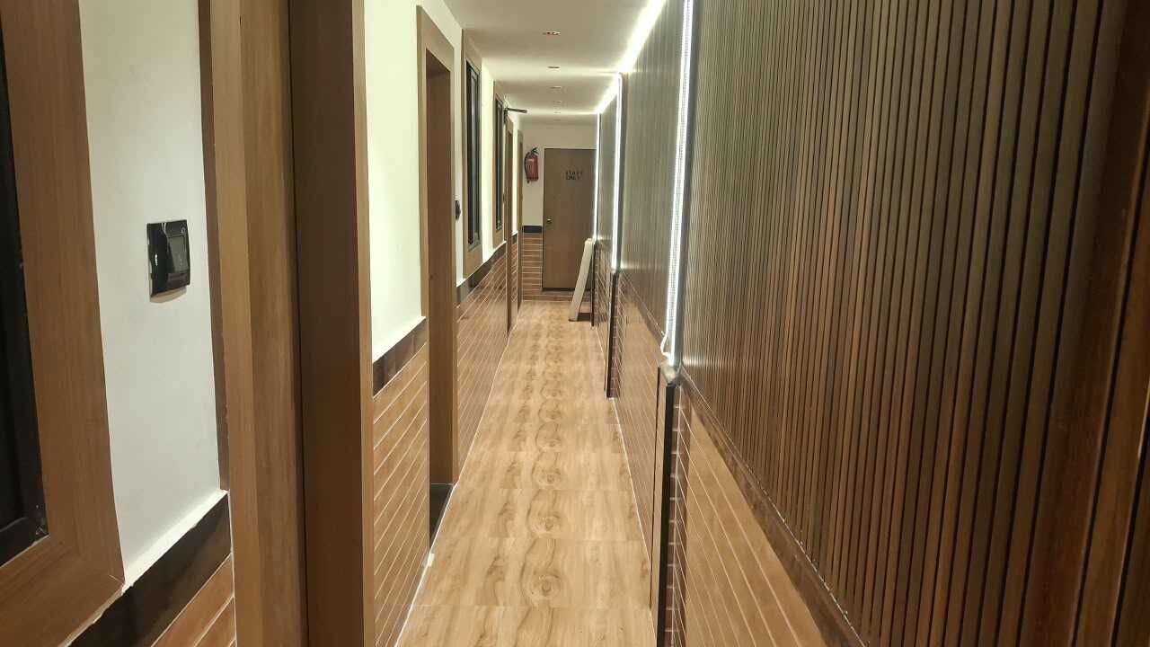A hotel corridor with wooden paneling on the walls, a tiled floor, and a door at the end.