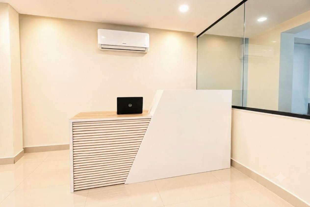 A reception desk with a laptop, a wall-mounted air conditioner, and a glass partition.