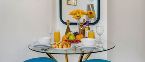 Una mesa de comedor con platos, vasos y una composición de frutas, frente a una pared blanca con un espejo y un letrero que dice 'BELLE'.