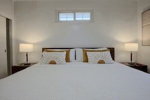 Quarto de hotel com uma cama grande, duas luminárias de cabeceira, uma janela e uma porta.