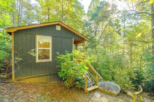 A small wooden cabin with a single window, surrounded by dense forest.