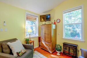 Una sala de estar con un sofá, un mueble de madera, un televisor y dos ventanas con persianas.