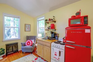 A kitchen with a red refrigerator, a stove, and a microwave. There is a chair and a window with a view of trees.