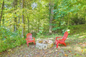 Two red Adirondack chairs facing a stone fire pit in a forested area.