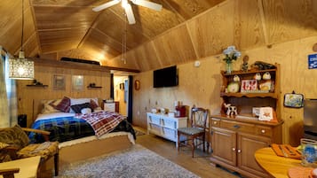 A cozy room with a bed, a desk, a chair, a television, and a ceiling fan.