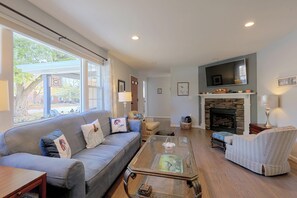 A spacious living room with a grey sofa, a glass coffee table, and a stone fireplace.
