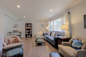 A living room with a sofa, armchairs, a coffee table, a bookshelf, and a window with curtains.