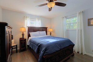 A bedroom with a wooden bed, two bedside lamps, a nightstand, a ceiling fan, and a window with curtains.