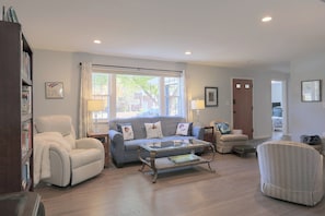 A spacious living room with a sofa, armchairs, a coffee table, and a bookshelf.