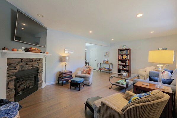 A living room with a stone fireplace, a television mounted on the wall, a bookshelf, and a comfortable seating area with a sofa and armchairs.
